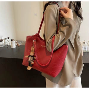 Macro detail of red textured leather tote bag featuring a cute bunny pendant accessory
