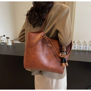 Detail of a brown leather tote bag with a small rabbit charm and logo in a cafe setting