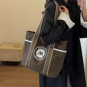 Bolso tote de lona marrón con ribete blanco y logotipo llevado por una modelo