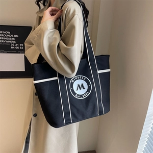 Bolso tote de lona negra con ribete blanco y logo, combinado con gabardina color beige