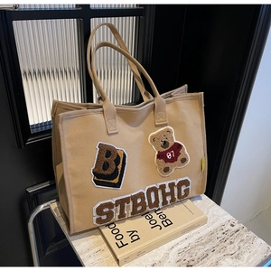 Close-up of khaki canvas tote bag featuring bear embroidery and chenille letter patches