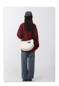 Close-up of white crescent canvas crossbody bag featuring adjustable black shoulder strap