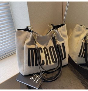 Detail of canvas tote bag with MICADLI patch, gold chain strap, and black leather trim