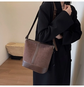 Brown suede patchwork bucket bag with adjustable strap worn by a model in a minimalist room