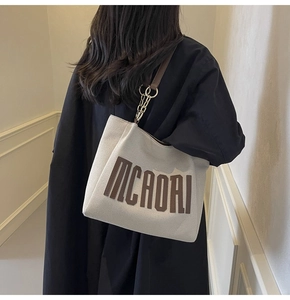 Detail of canvas tote bag with brown leather straps and metal chain accents for women