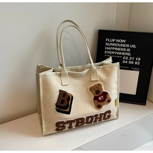 Detail of canvas tote bag featuring plush teddy bear patch and letter B embroidery