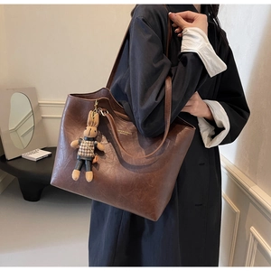 Brown leather tote bag featuring a plush bunny pendant and gold fashion lettering