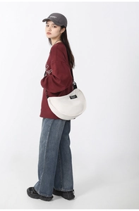 Detailed view of white nylon crescent bag with adjustable black shoulder strap and zipper
