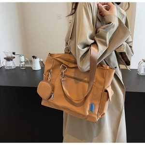 Detail of khaki nylon tote bag featuring functional zippers and a round coin pouch accessory