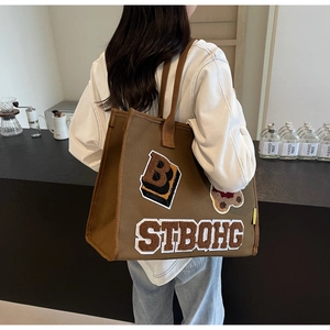 Brown canvas tote bag with embroidered bear and letter patches shown on shoulder