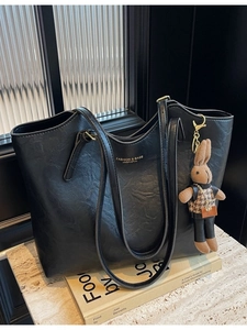 Black leather tote bag with rabbit pendant on a modern minimalist marble background