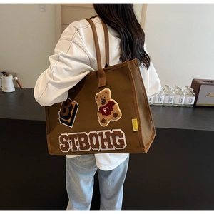 Detail of dark brown canvas tote bag with embroidered teddy bear and vintage college patches