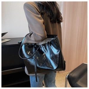 Side view of large black glossy pleated leather tote bag shown on model for shoulder wear