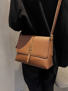 Braune Leder-Umhängetasche mit Goldschnalle auf schwarzem Anzug für minimalistisches Pendeln
