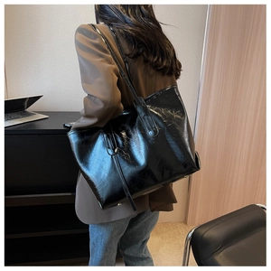 Detailed view of black patent leather tote bag with glossy cracked texture on a model