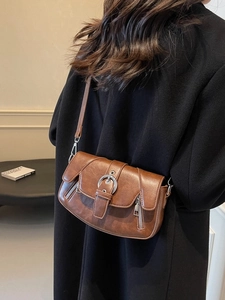 Vintage brown leather saddle bag with buckle and zipper detail worn over black coat