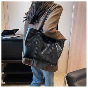 Detail of a large black glossy tote bag with pleated leather texture worn by a model