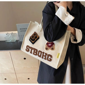 Detail of canvas tote bag featuring plush bear embroidery and large Strong lettering