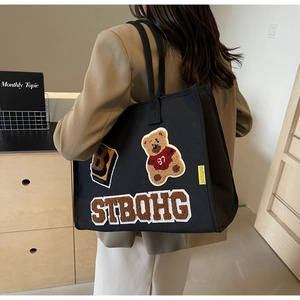 Detail of black canvas tote bag featuring teddy bear embroidery and large letter B patch