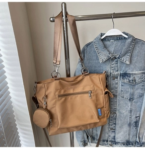 Detail of a brown nylon tote bag featuring a front zipper pocket and round coin purse accessory