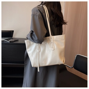 Lifestyle shot showing a large off-white crinkled patent leather tote bag on shoulder