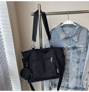 Detailed view of a black nylon tote bag featuring side buckle pockets and a small round coin purse
