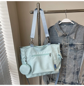 Detail of light blue tote bag featuring a front zipper pocket and a small coin purse charm