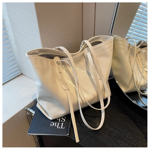 Detail of a creamy white tote bag featuring glossy crinkled faux leather and long straps