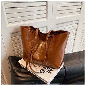 Brown large capacity tote bag with oil wax leather texture on a white book surface