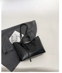 Detail of black tote bag featuring glossy oil wax leather texture and metal base studs