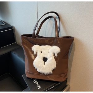 Détail du sac cabas marron avec écusson chien en peluche posé sur un magazine de mode