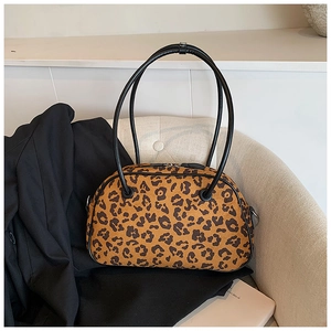Detail der Handtasche mit Leopardenmuster auf beigem Sofa neben einem Modebuch