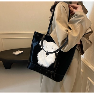Détail du sac cabas noir brillant avec un patch chiot en peluche et de fines anses
