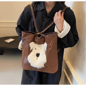Sac fourre-tout en cuir marron avec motif chiot en peluche porté sur un manteau noir