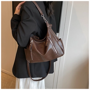 Detail of dark brown leather hobo bag with multiple zippers shown on shoulder