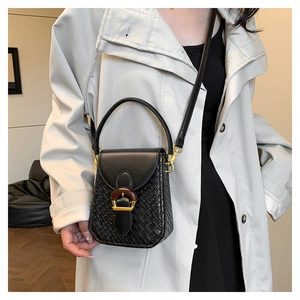 Detail of crossbody bag featuring smooth leather, woven texture, and wood grain buckle