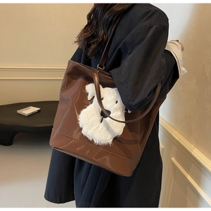 Sac cabas marron brillant avec écusson de chiot en peluche, porté comme un grand sac