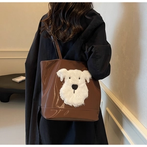 Détail d'un sac cabas en cuir marron brillant avec patch chien en peluche sur un mannequin
