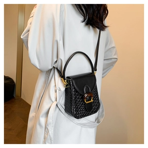 Detail of a structured black crossbody bag with woven texture and a wood-grain buckle