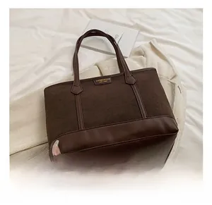 Detail of dark brown tote bag showing matte and smooth leather patchwork with metal logo