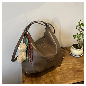 Brown faux leather tote bag with plush bear charm and woven rope detail on a wooden table
