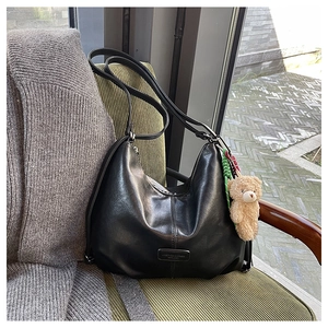 Close-up of a black leather tote bag with a plush bear charm on a striped green chair