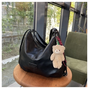 Detail of black pebbled PU leather tote bag with a cute beige teddy bear charm on wood stool