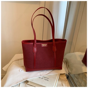 Detail view of burgundy tote bag with gold lettering over a book and white blazer