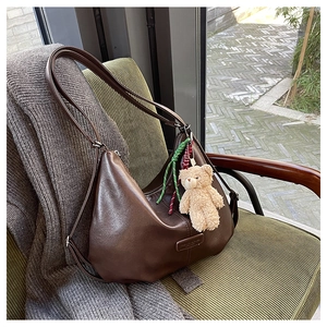 Detail of dark brown leather hobo bag with teddy charm on green corduroy chair