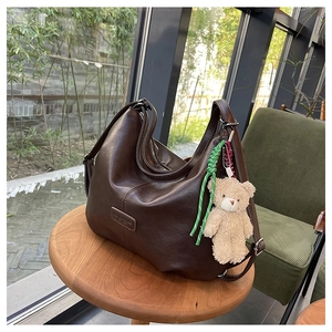 Detail of deep brown leather tote bag with wide strap and a cute mini plush bear charm
