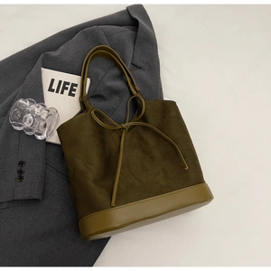 Detail of olive green bucket bag with suede texture and bow drawstring on grey suit