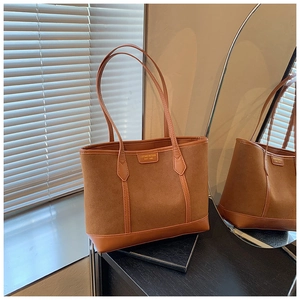 Detail of a brown tote bag with suede and smooth leather texture with metal brand tag