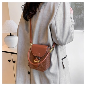 Close-up of brown woven leather crossbody bag with gold ring buckle on a grey blazer