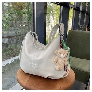 Detailed close-up of cream leather tote bag with decorative bear charm on wooden stool